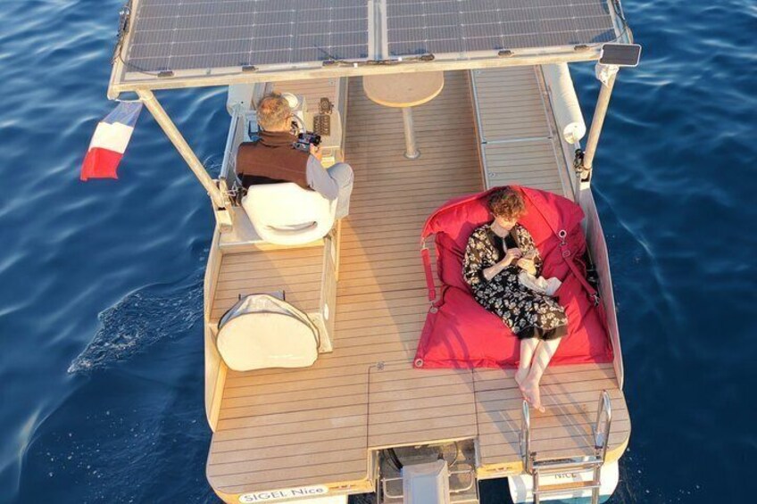 A boat with a person sitting on a red cushion, another person taking a photo, and a French flag. 3