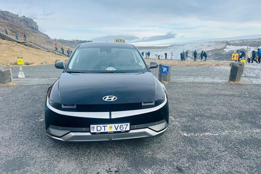 Un'auto Hyundai nera con segnale da taxi sul tetto, parcheggiata su una strada con un paesaggio montuoso sullo sfondo. 4