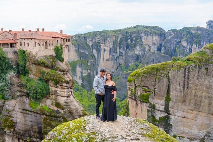 A couple standing on a rock with a castle and cliffs in the background. 5