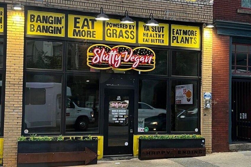 Un escaparate con un letrero que dice 'Slutty Vegan' y lemas como 'Come más' y 'Impulsado por la hierba'. 2