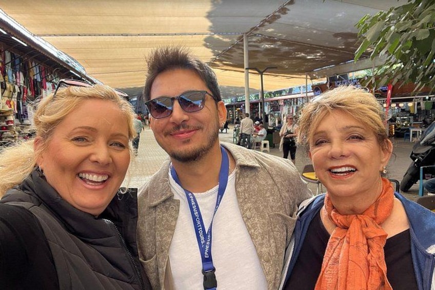 Tres personas en un mercado al aire libre con puestos y un toldo. 1