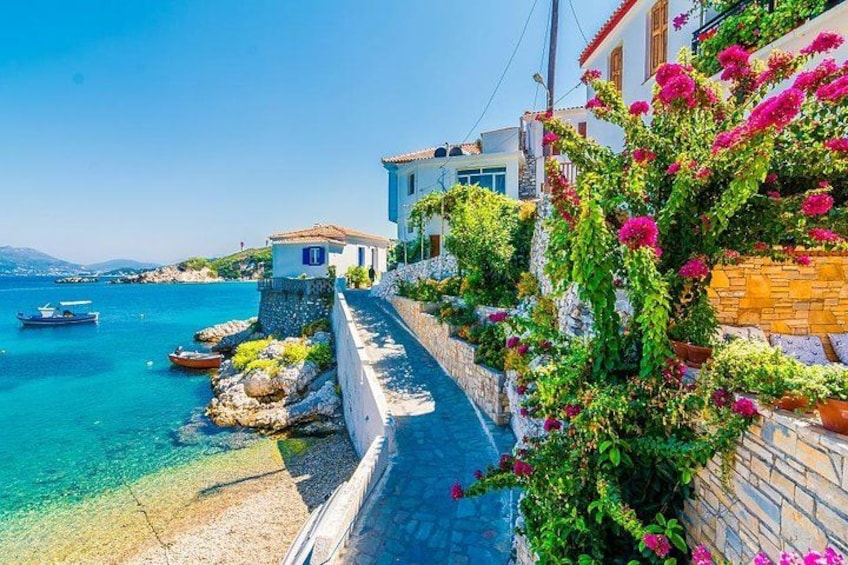 A coastal street with buildings, a clear blue sea, and boats. 1
