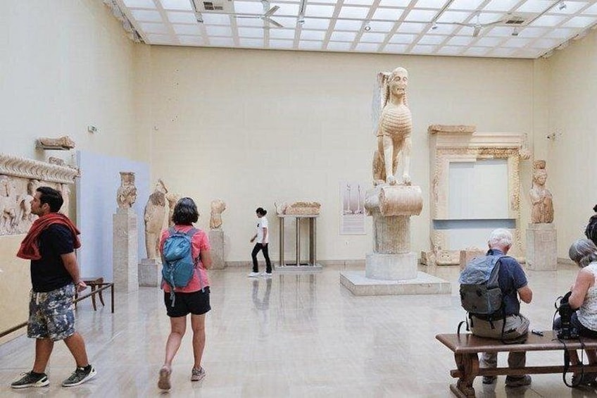 An indoor museum with visitors observing ancient sculptures and a large central statue. 5