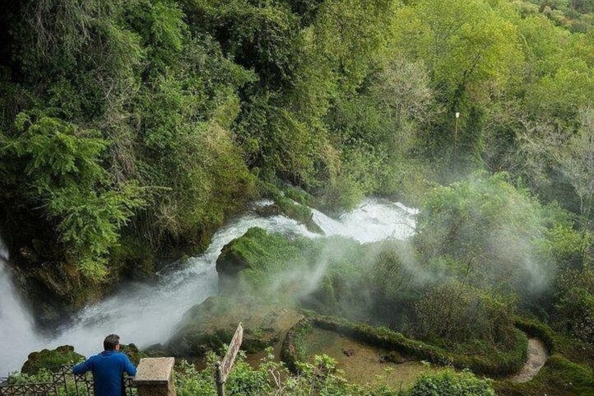 Une cascade située dans une zone boisée, avec une personne qui l'observe de loin. 2