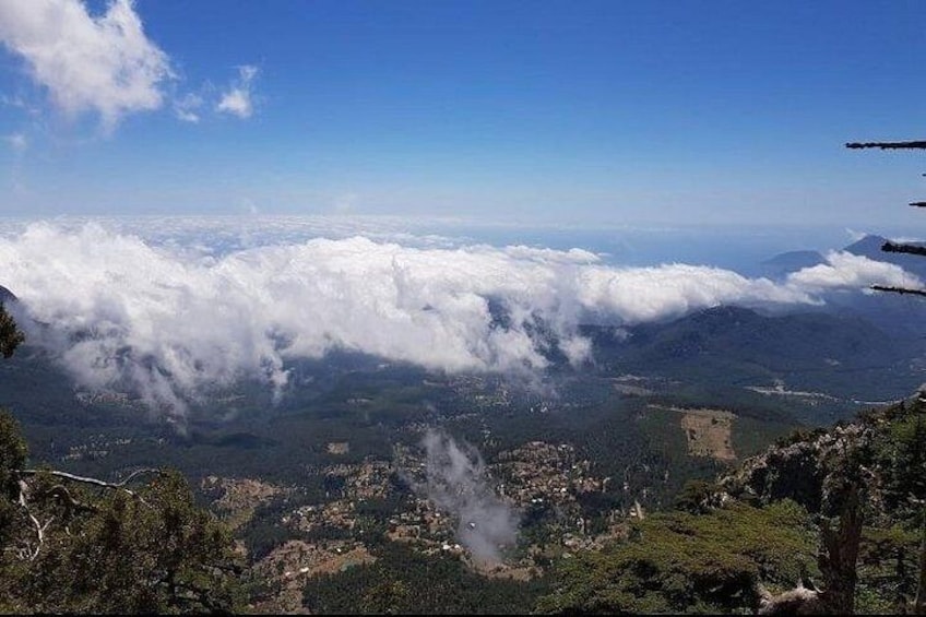 A mountainous landscape with a view of clouds below and a village in the valley. 5