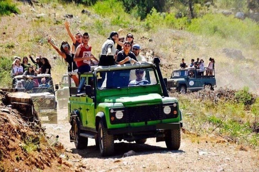 A green off-road vehicle with passengers on a dirt road surrounded by dry grass and shrubs. 1
