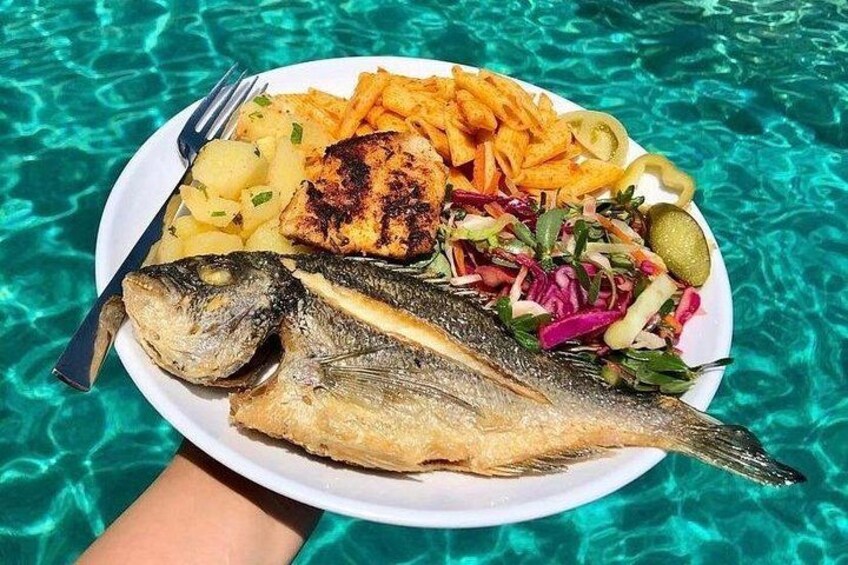 A plate of grilled fish, fries, and salad with a poolside setting. 4