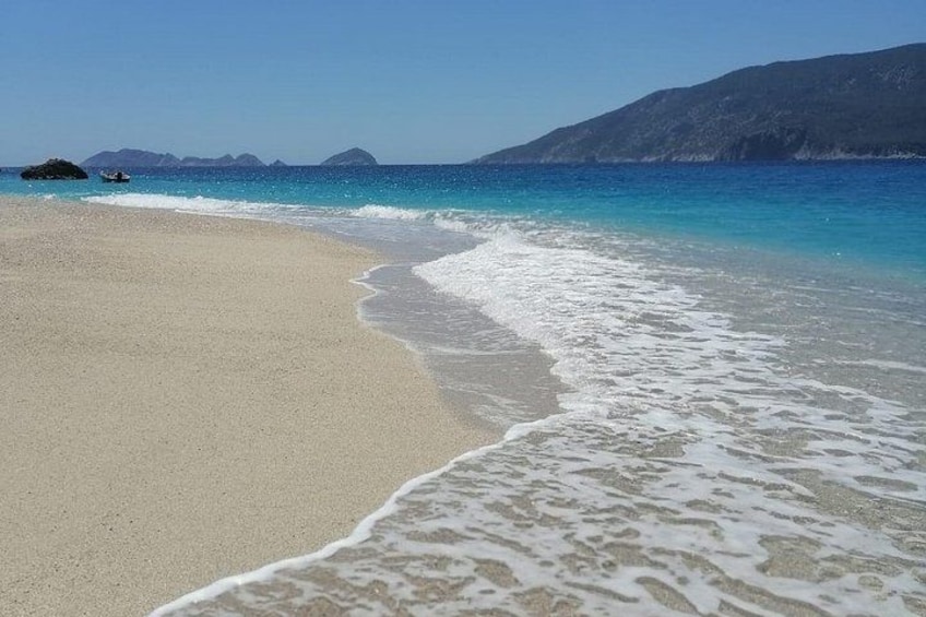 A beach with clear turquoise water, gentle waves, and distant rocky islands. 3