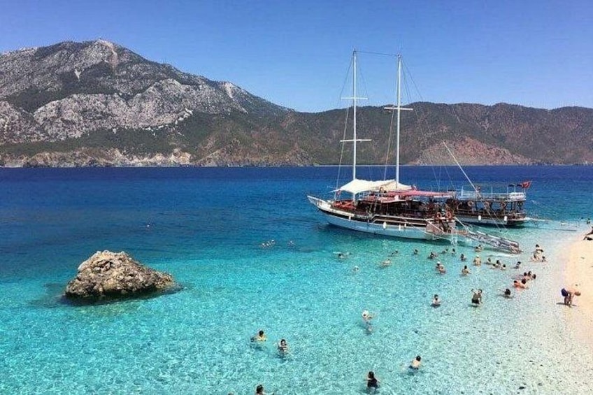 A beach with clear turquoise water, a rocky outcrop, and a sailboat anchored near the shore. 5