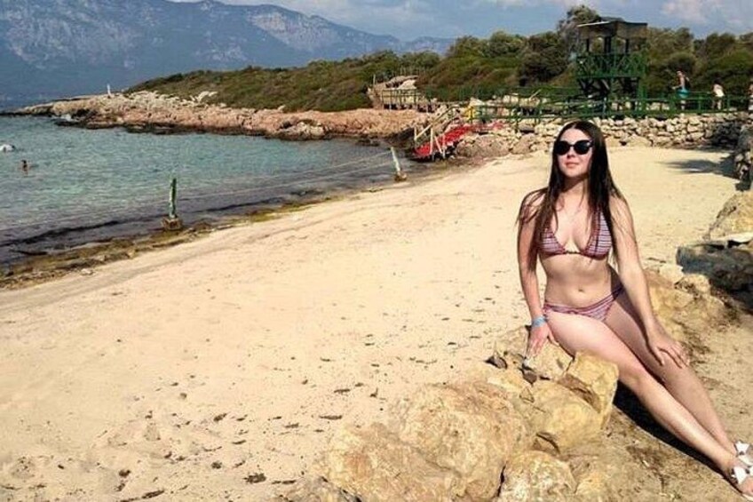 A beach with clear water, rocky shore, and a person sitting on a rock. 4
