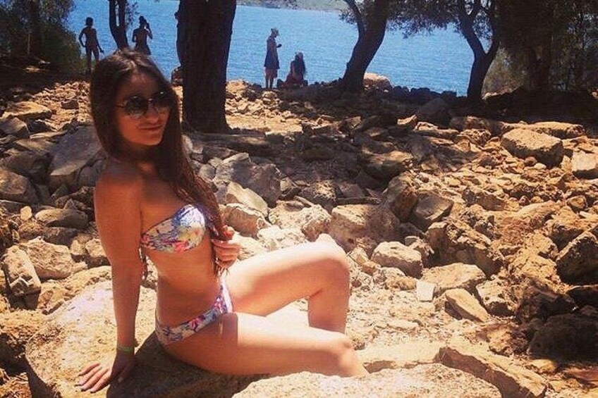 A person sitting on rocks near a body of water with trees in the background. 2