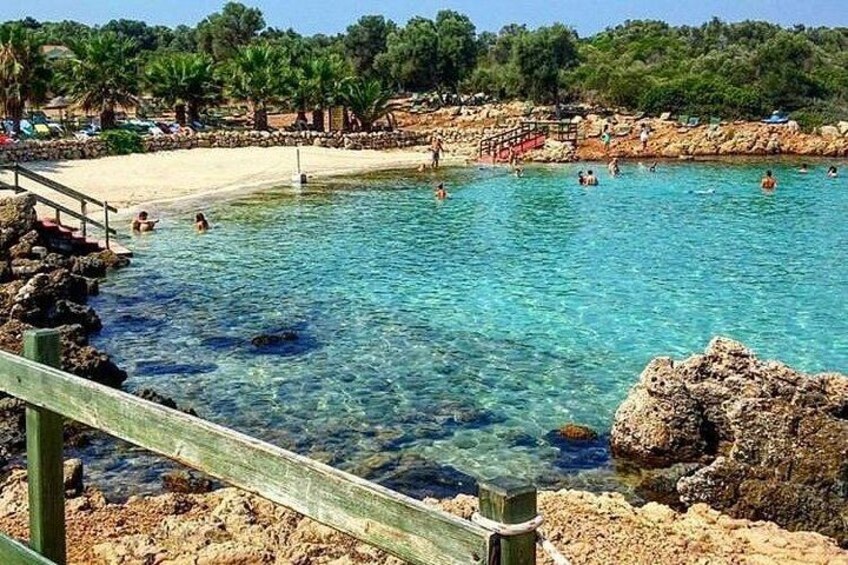 A clear blue pool surrounded by rocky terrain and a sandy beach with people swimming. 5