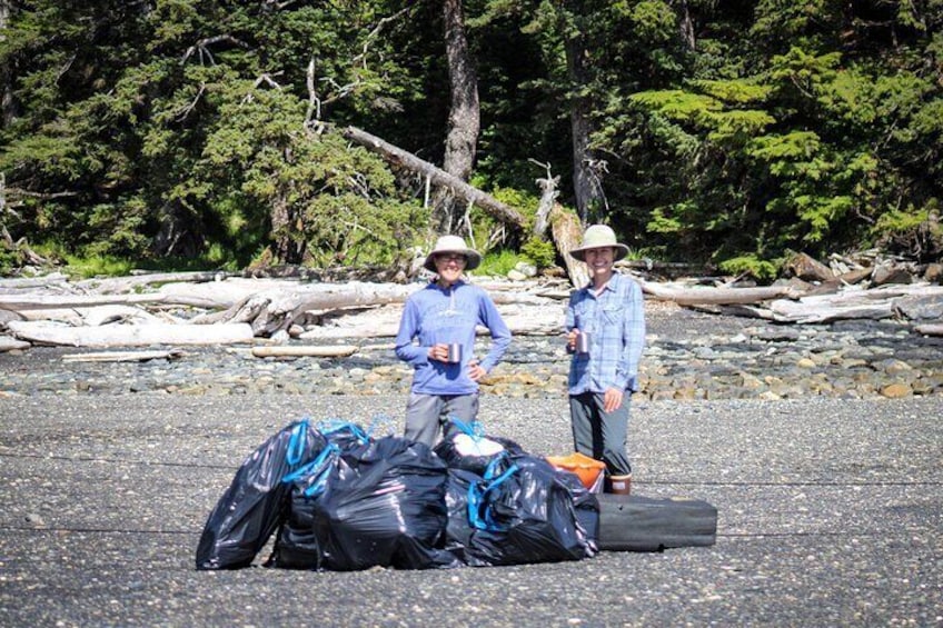 Two people standing on a rocky beach with bags and a suitcase. 5