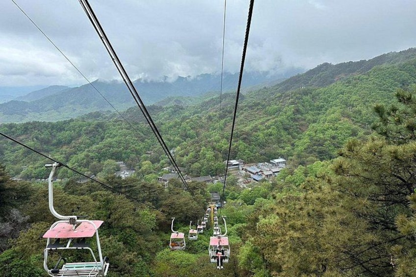 A cable car system in a mountainous area with lush greenery and distant buildings. 3