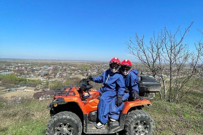 Dos personas con trajes protectores azules y cascos rojos sobre un vehículo todo terreno naranja. 3