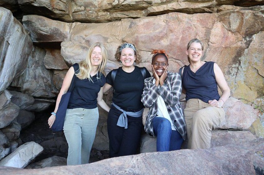Four people standing and sitting in front of a rocky cave entrance. 5