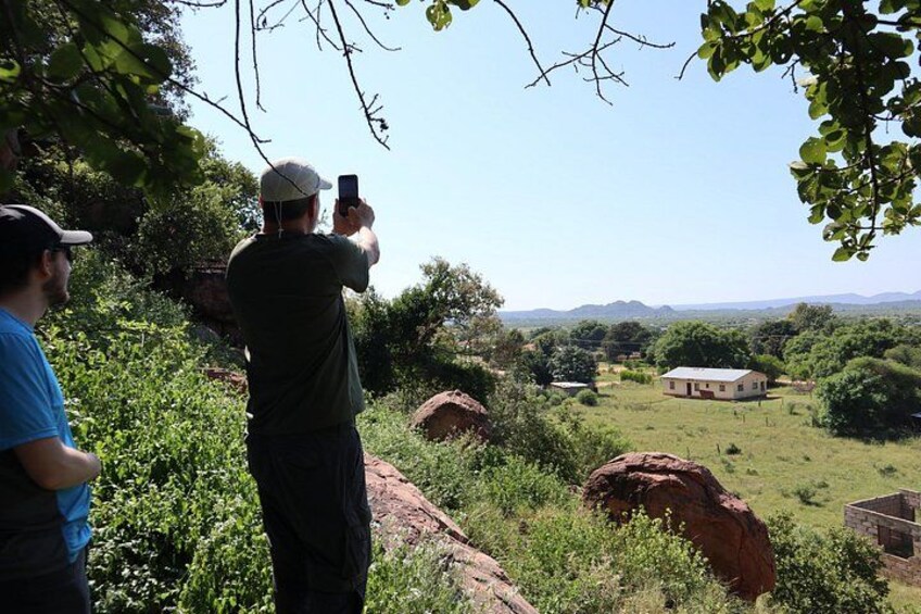 A person taking a photo of a rural landscape with a house, trees, and a clear sky. 3