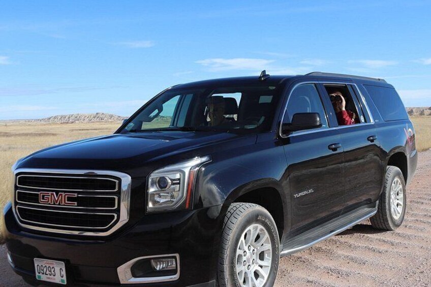 Un SUV GMC Yukon XL noir est garé sur un chemin de terre, avec un ciel dégagé en arrière-plan. 2