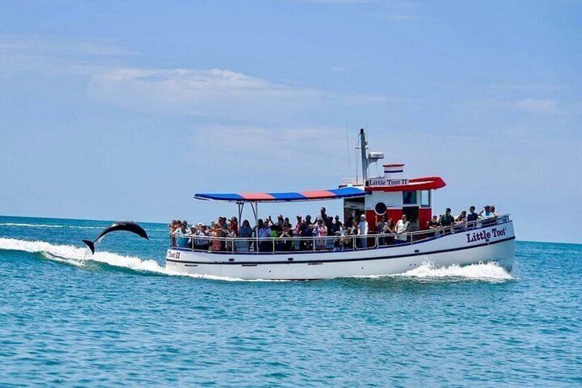 Een boot genaamd 'Little Tour' met passagiers, een wakeboarder en een strakblauwe lucht. 1