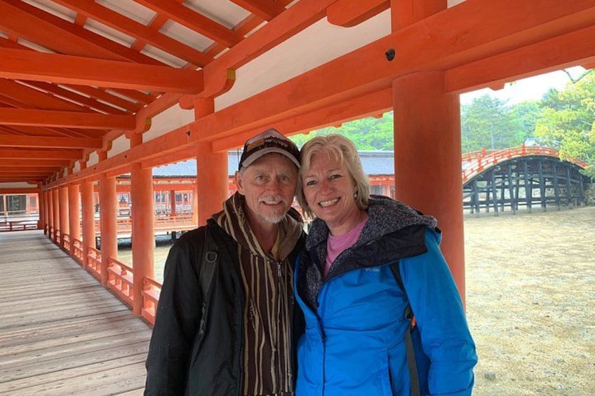 A covered walkway with orange pillars and a wooden deck, leading to a traditional Japanese structure. 3