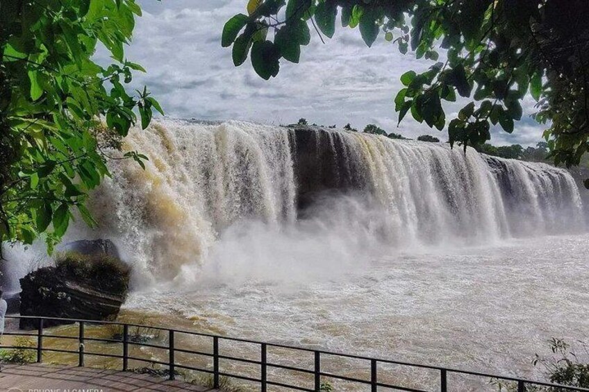 A waterfall cascading over rocks, surrounded by greenery and a metal railing. 2
