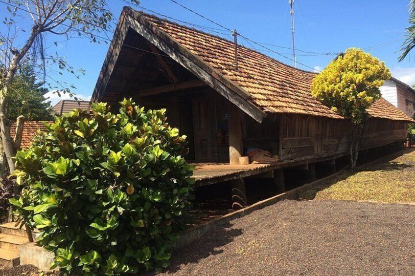 A wooden house with a sloped roof, a large bush in the foreground, and a clear blue sky. 5