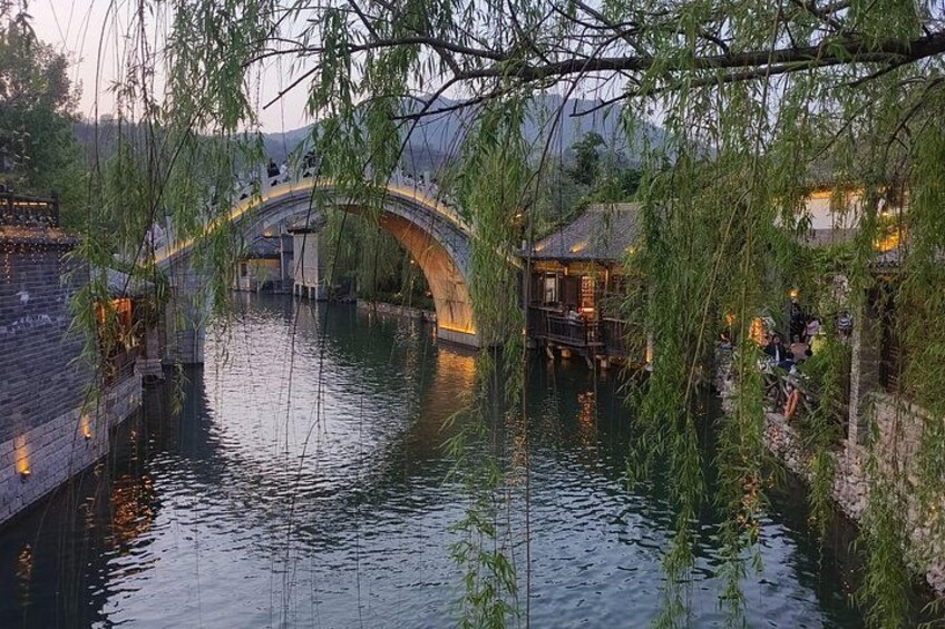 Un pont de pierre enjambant une rivière paisible, entouré d’une végétation luxuriante et de bâtiments traditionnels. 3