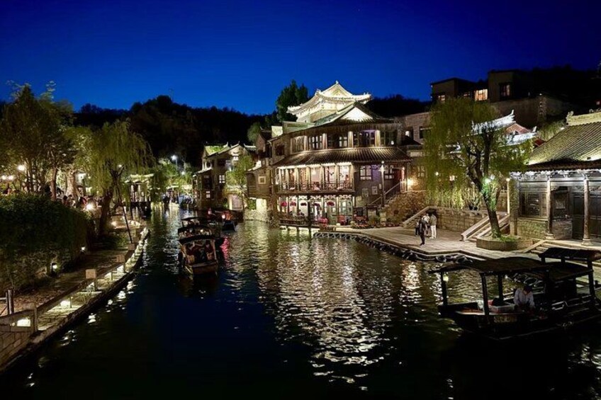 A river with traditional buildings, a boat, and a pedestrian walkway at night. 2