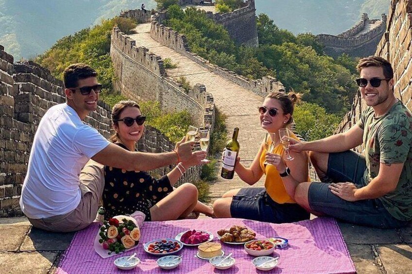 A group of people toasting with wine on a blanket at the Great Wall of China. 2