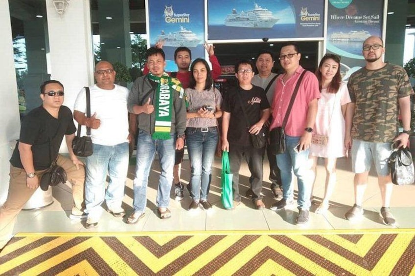 A group of people posing in front of a building with a large poster of a cruise ship. 2