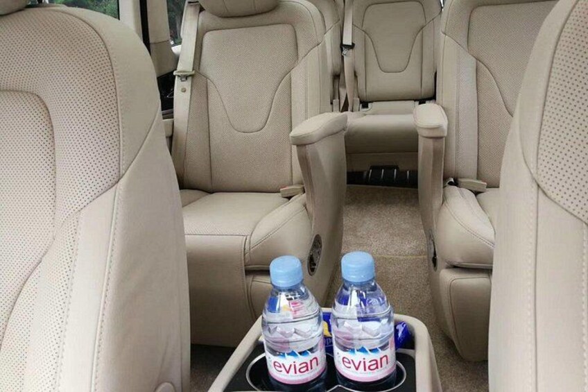 A vehicle interior with beige leather seats and a center console holding two Evian water bottles. 1