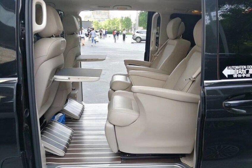 A vehicle interior with beige seats, a foldable table, and a rear storage compartment. 3