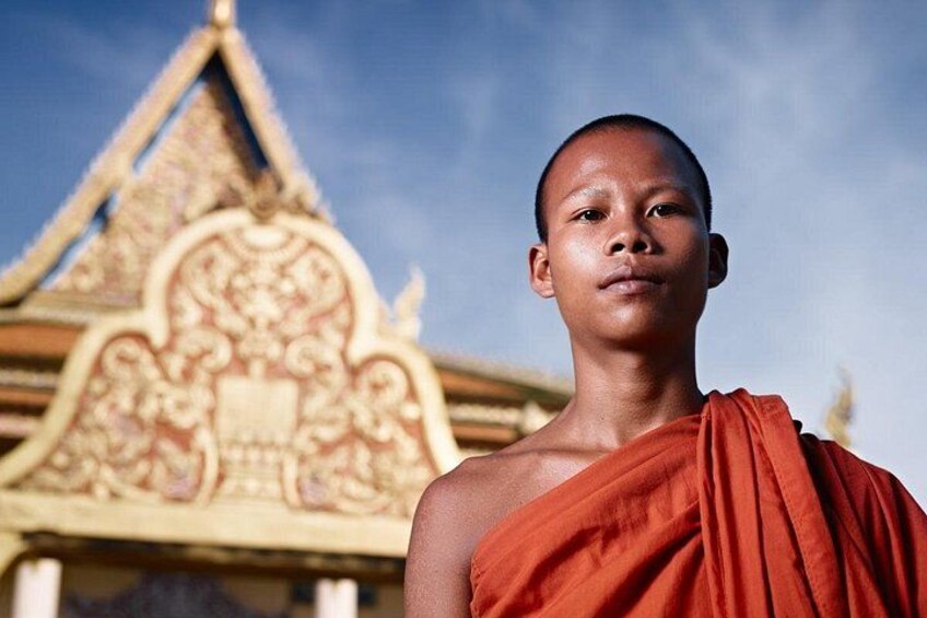 A person in a traditional orange robe standing in front of a temple with intricate architectural details. 2