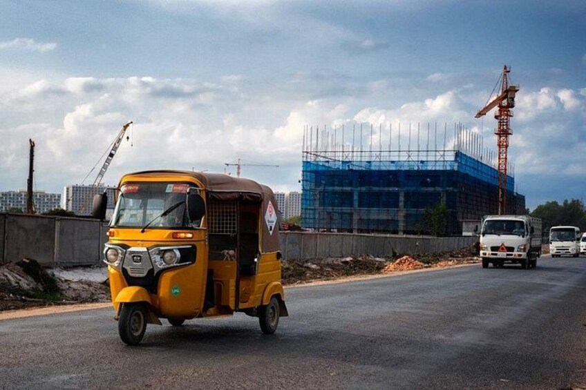 A yellow auto-rickshaw on a road with a construction site and a building under construction in the background. 3