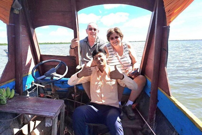 Een houten boot met drie personen aan boord, een stuurwiel en bananen op het dek. 4
