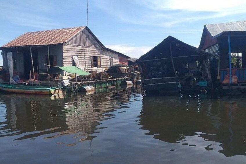 A floating house with a green canopy, a docked boat, and a calm water body. 5