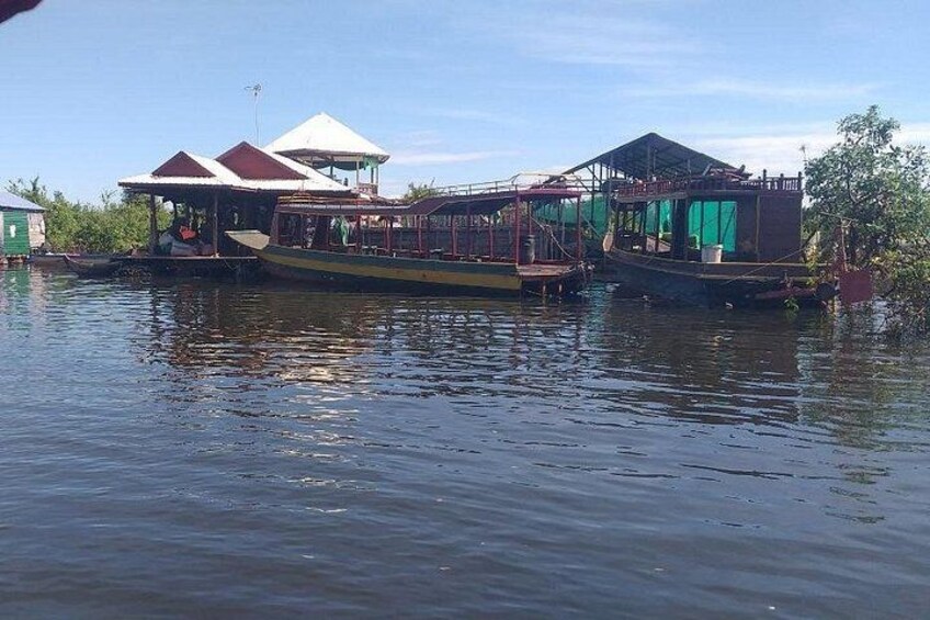 A floating houseboat with a covered deck and a green canopy, docked in calm water. 2