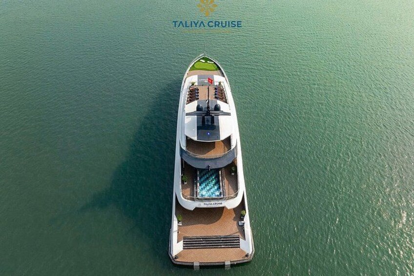 En stor, hvid yacht med et grønt dæk, døbt 'TALIIA CRUISE', der flyder på roligt vand. 5