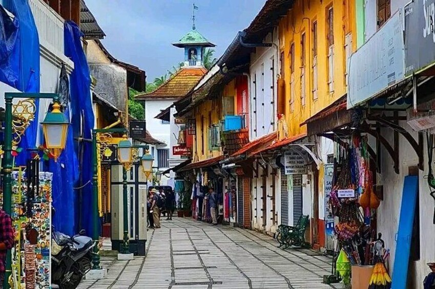 Una calle estrecha flanqueada por edificios de colores, una torre del reloj y diversas tiendas. 2
