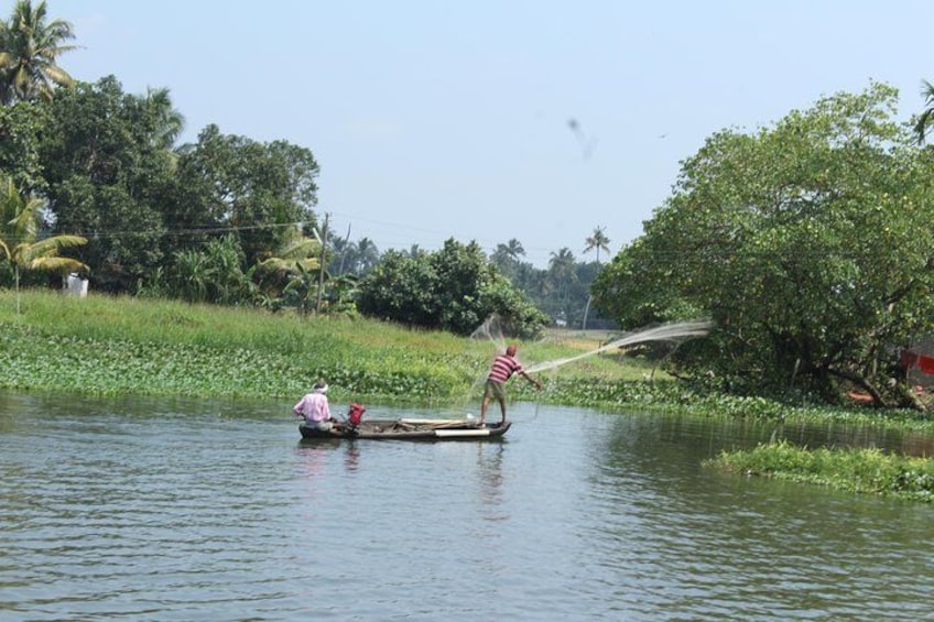 Ein Mann paddelt in einem Boot auf einem ruhigen Fluss, umgeben von üppiger Vegetation und Palmen. 2