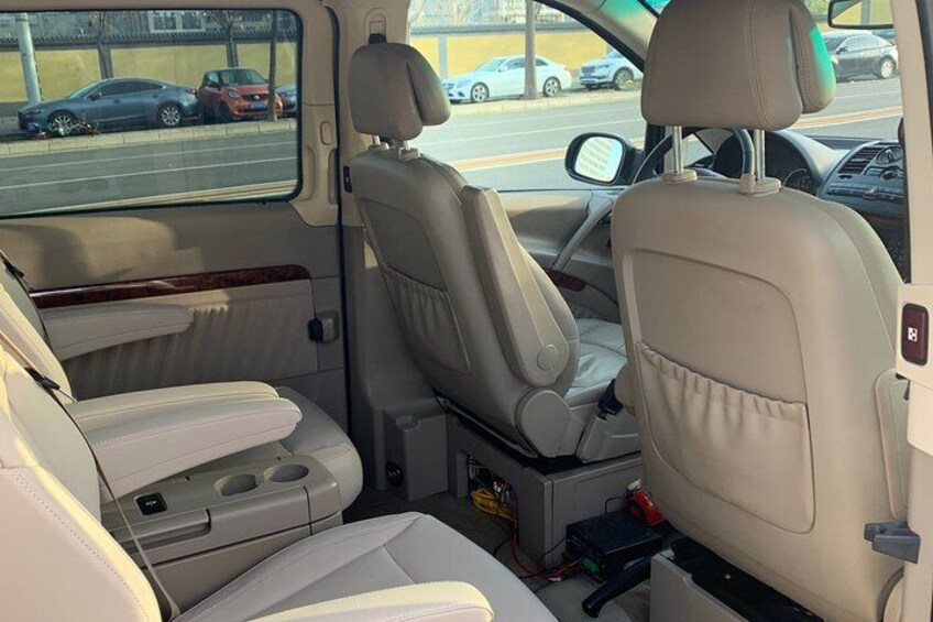 The interior of a vehicle with beige leather seats, a center console, and a rearview mirror. 1
