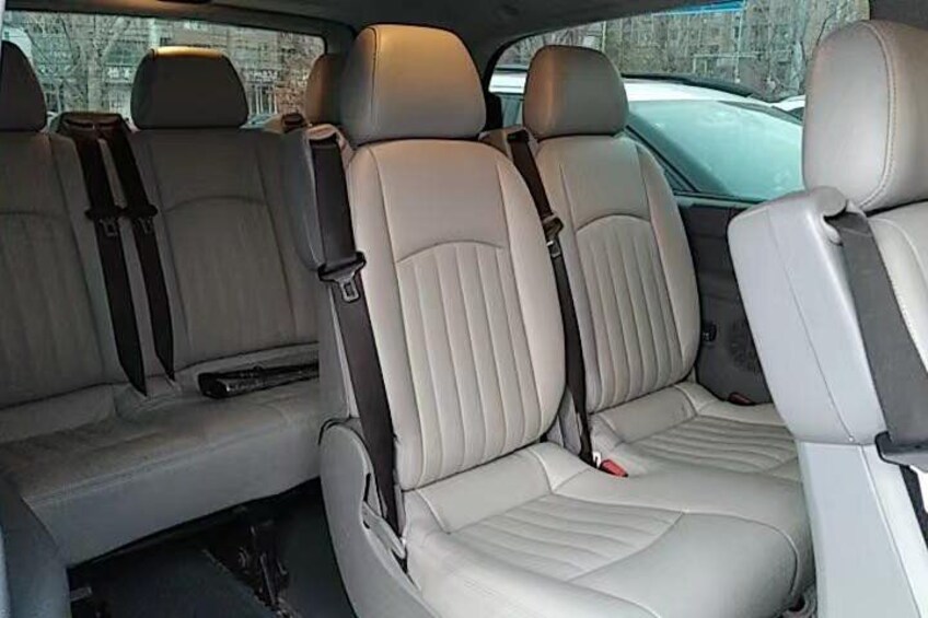 A car interior with beige leather seats, seat belts, and a center console. 2
