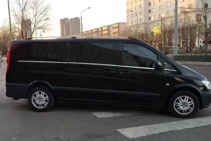 A black van parked on a city street with buildings and trees in the background. 4