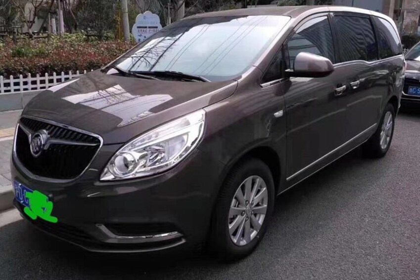 A dark-colored SUV parked on a street with a white fence and trees in the background. 5