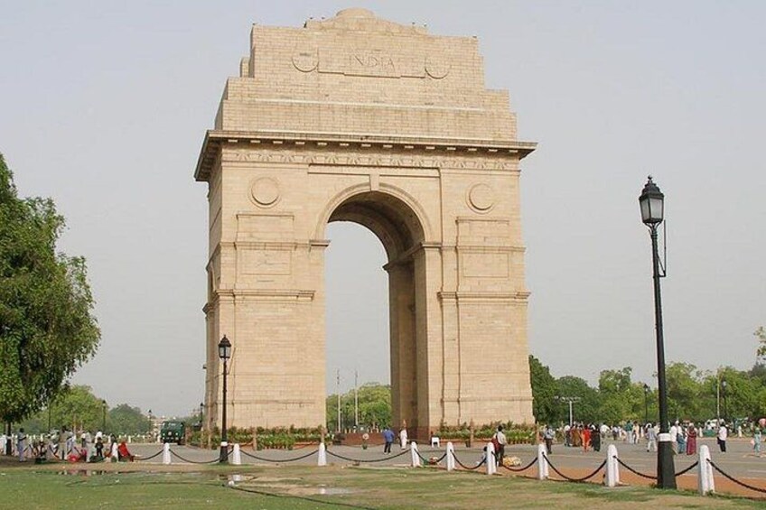 A large stone arch monument with inscriptions, surrounded by a paved area with people and trees. 1