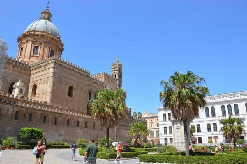 A historic building with a dome and a bell tower, surrounded by palm trees and a well-maintained garden. 3