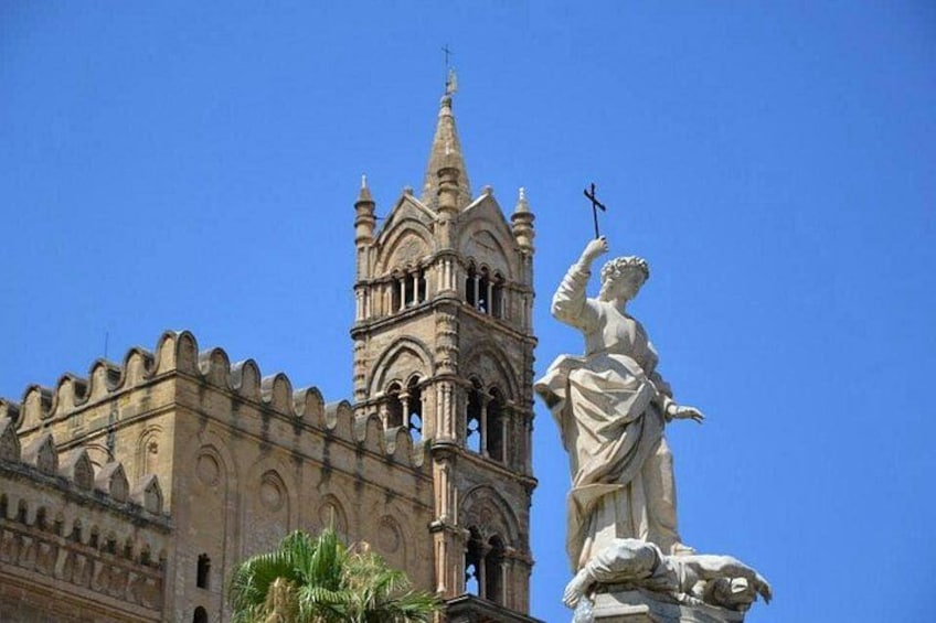 A historic building with a prominent tower and a statue of a robed figure holding a cross. 5