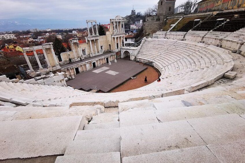 An ancient amphitheater with stone steps and a central stage. 1