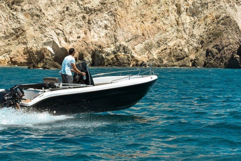 A motorboat on water with a rocky coastline in the background. 4