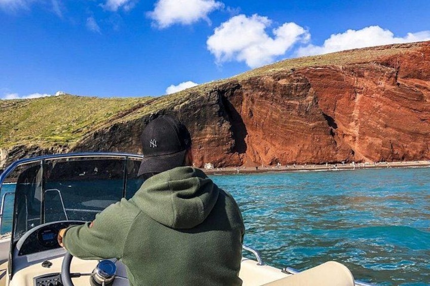A person driving a boat on a body of water with a red rock formation in the background. 2